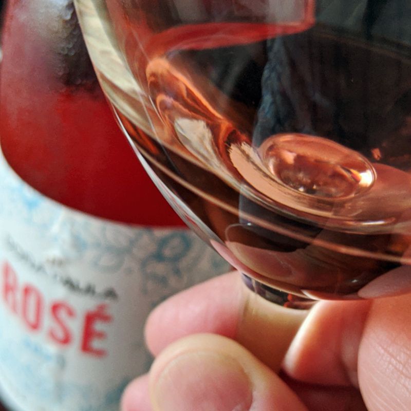 Copa de Doña Paula Rosé 2020 en mano con imagen de botella en el fondo